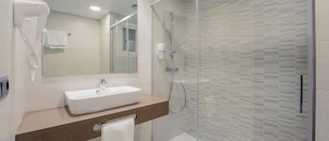 A modern bathroom with a glass-enclosed shower, a white sink, and a hairdryer mounted on the wall.