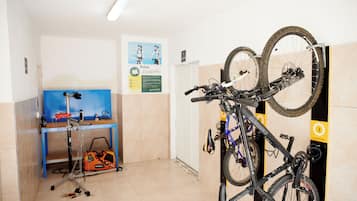 Una habitación con un aparcamiento para bicicletas con dos bicis, un escritorio azul con una computadora y un cartel en la pared.