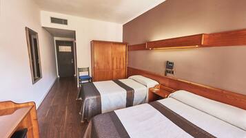 A hotel room with two beds, a wooden wardrobe, a desk, and a chair.
