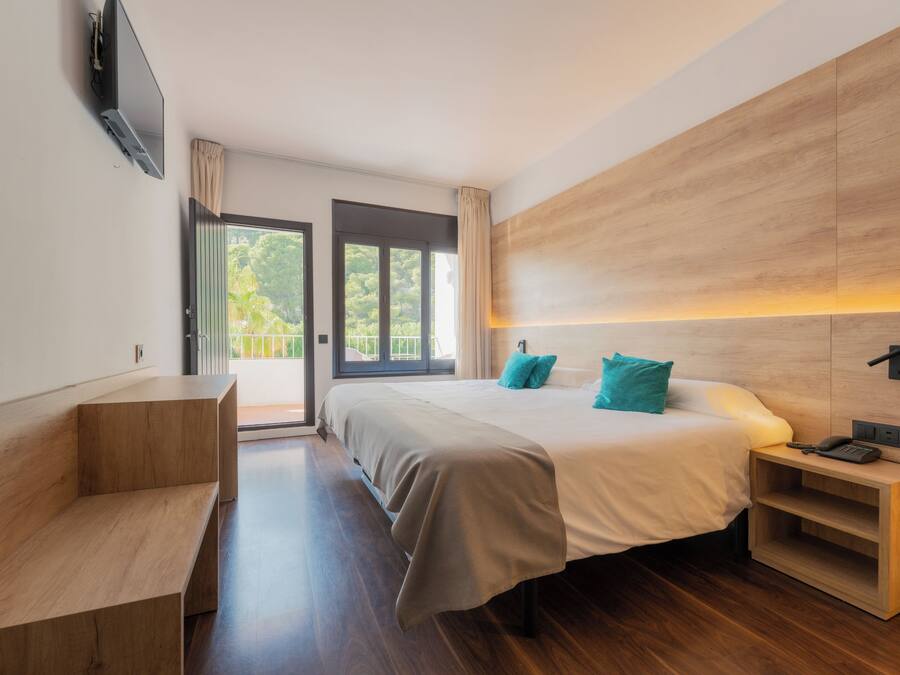 Ein modernes Hotelzimmer mit einem großen Bett, einer Holzbank, einem Nachttisch mit Telefon und einem an der Wand montierten Fernseher.
