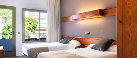 A hotel room with two beds, a wooden headboard, a window with curtains, and a view of greenery outside.