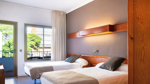 Une chambre d’hôtel avec deux lits, une tête de lit en bois, une fenêtre avec des rideaux et une vue sur la verdure.