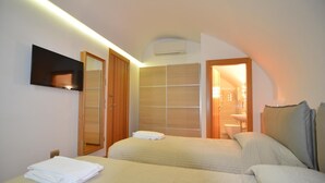 Habitación de hotel con dos camas, televisión, espejo y baño visible a través de una puerta abierta.