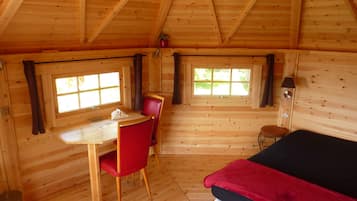 A wooden cabin room with a bed, a table, and two chairs.