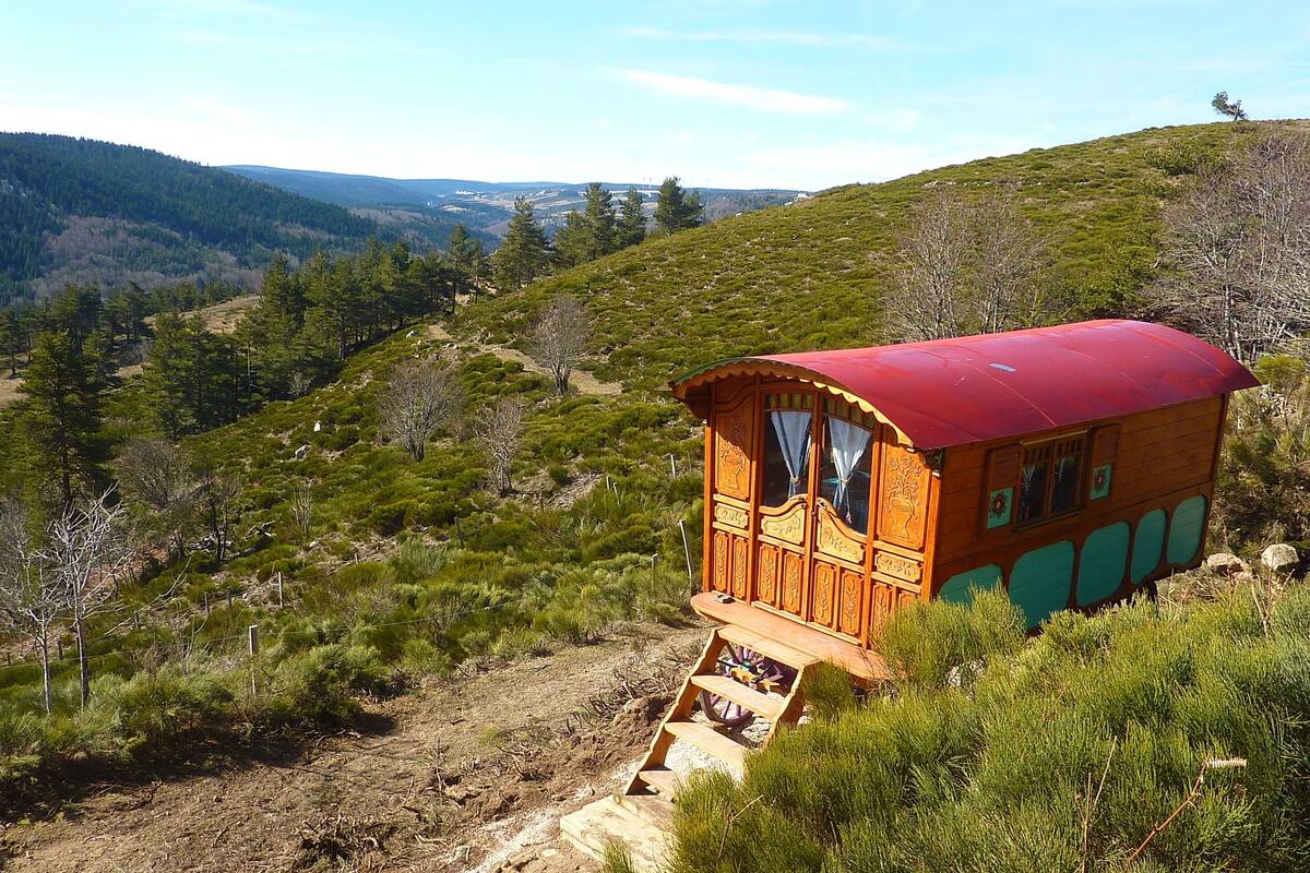 A wooden cabin with a red roof, situated on a hillside with a view of the surrounding landscape.