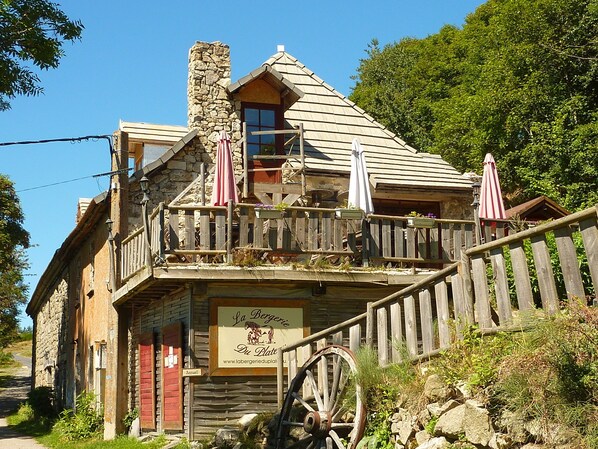A rustic wooden building with a balcony, stone chimney, and a sign reading "La Bergerie Du Plate".