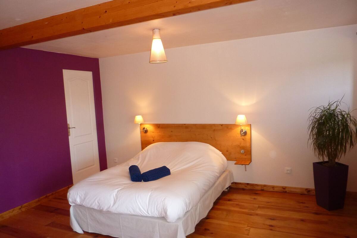 A bedroom with a wooden headboard, a bed with white bedding, a potted plant, and a wooden floor.