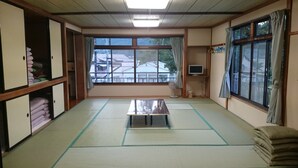 A tatami mat room with a tatami mat table, a television, and a window with curtains. - Yagisakien (Fujikawaguchiko)