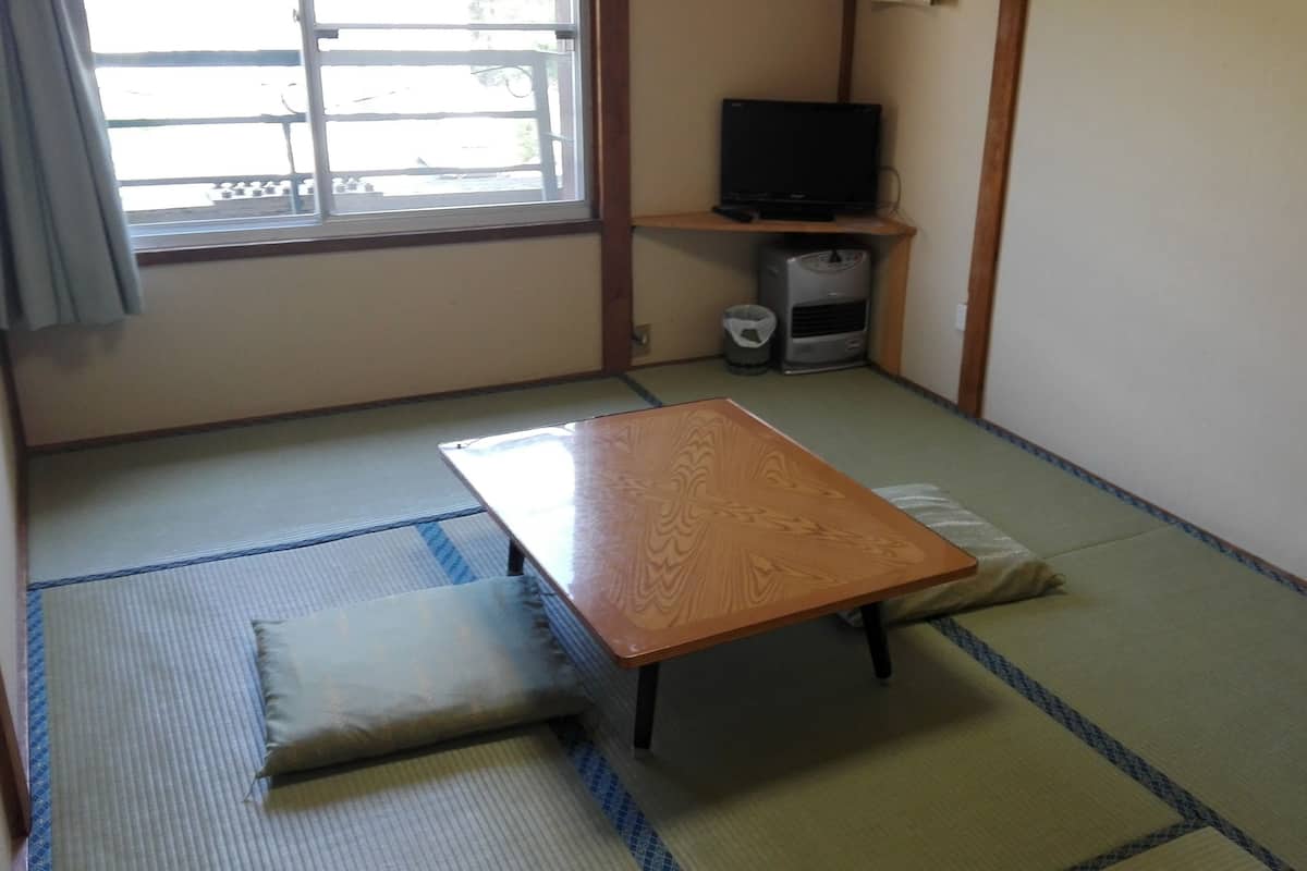 A room with tatami mat flooring, a wooden table, and a television on a shelf.