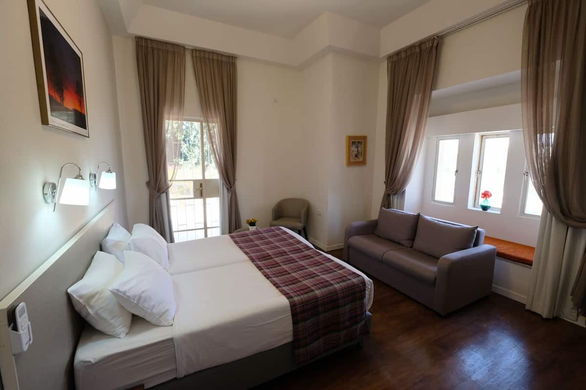 A hotel room with a bed, a sofa, a chair, and a window with curtains.