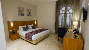 A hotel room with a large bed, a desk with a TV, a chair, and artwork on the wall.