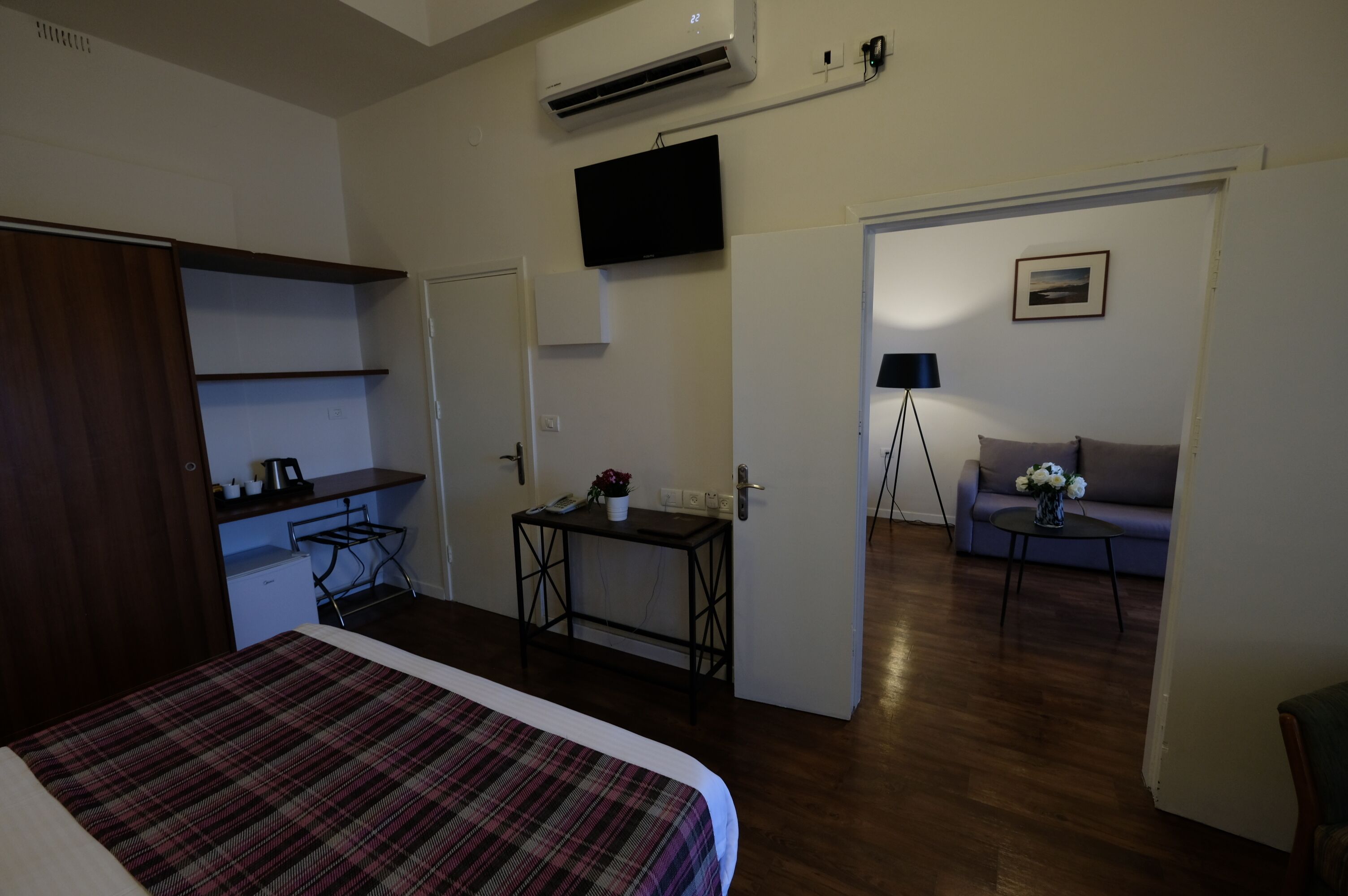 A hotel room with a bed, a desk, a chair, a sofa, a television, and a picture on the wall.