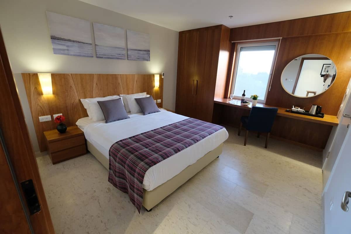 A bedroom with a bed, bedside tables, a desk, a chair, a mirror, and artwork on the wall.