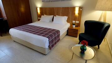 Quarto de hotel com uma cama, mesas de cabeceira, uma cadeira e uma pequena mesa com um vaso.