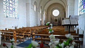 Interior de una iglesia con hileras de bancas de madera, un pasillo central y un amplio vitral.