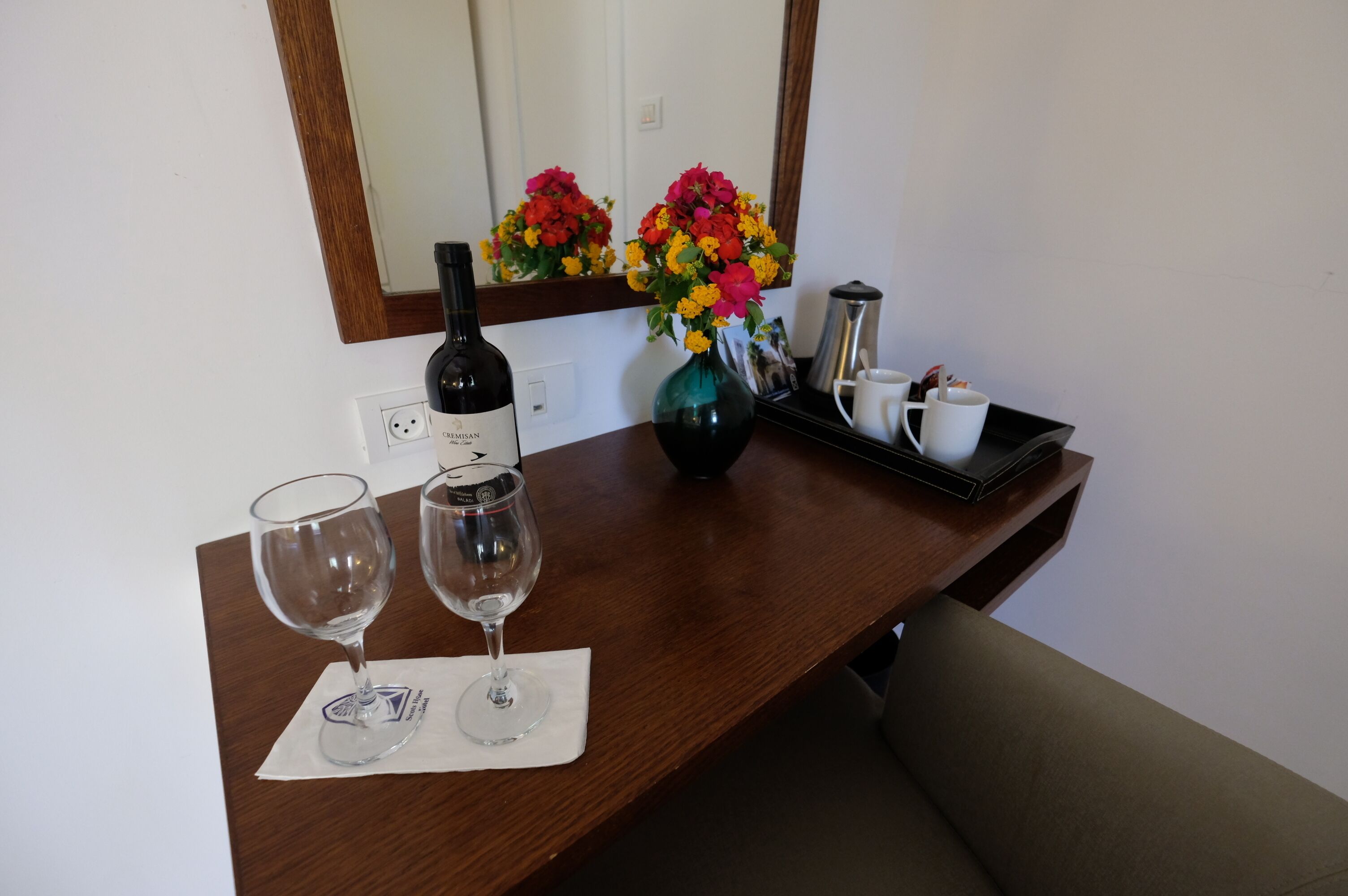 A wooden table with two wine glasses, a bottle of wine, a vase with flowers, and a coffee maker.