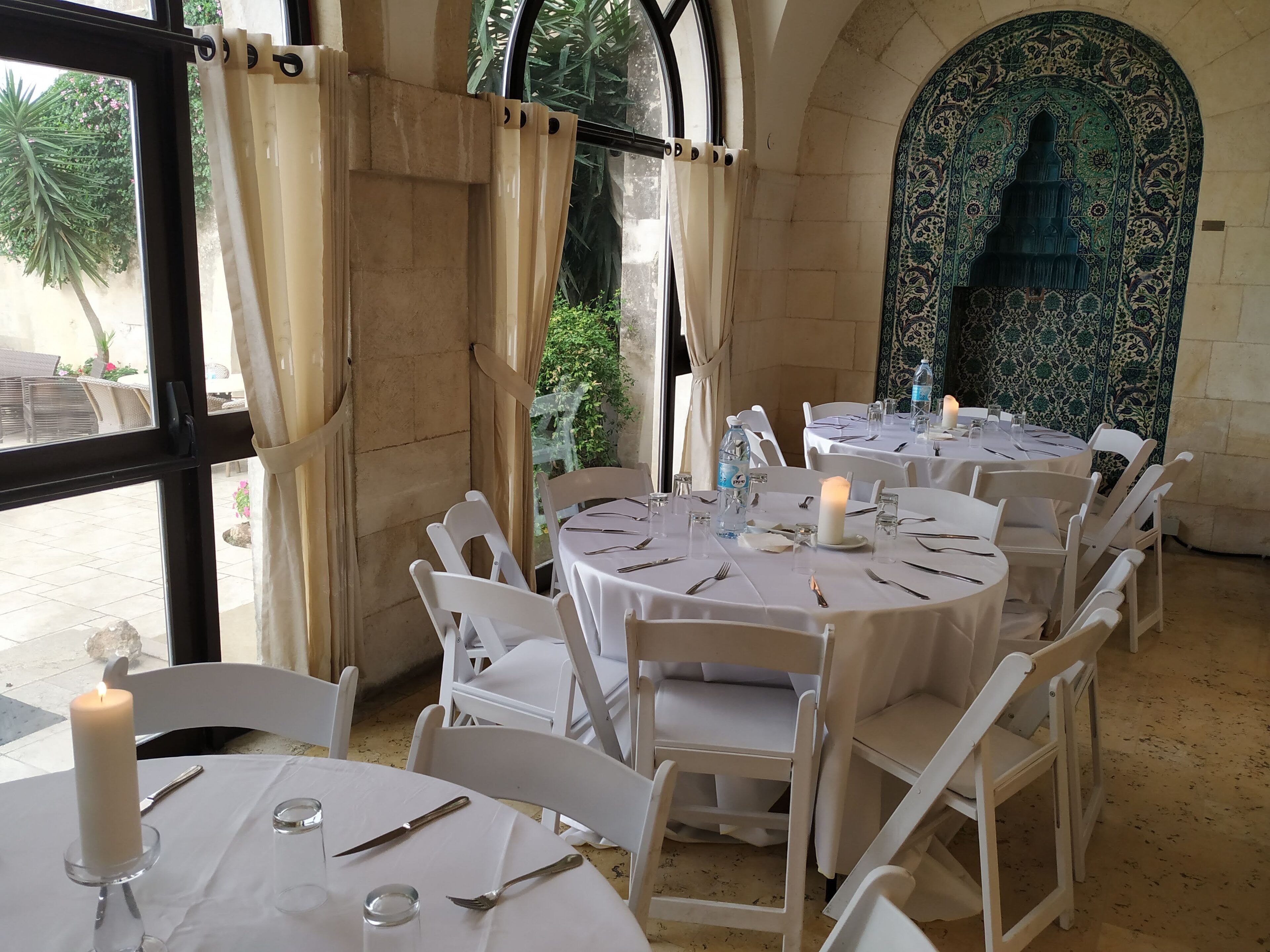 Un espace repas avec des tables rondes, des chaises blanches et des bougies.
