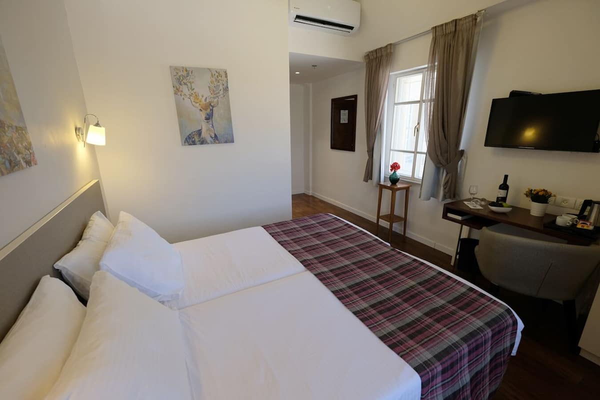 A hotel room with a bed, a desk with a chair, a television, and a window with curtains.