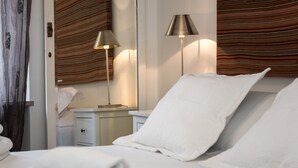 Ein Hotelzimmer mit einem ordentlich bezogenen Bett, einem Nachttisch mit Lampe und gestreiften Vorhängen.
