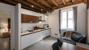 Eine moderne Küche mit weißen Schränken, einer Mikrowelle und einem Herd. Im Wohnbereich befindet sich ein Fenster mit Vorhängen und eine Couch.