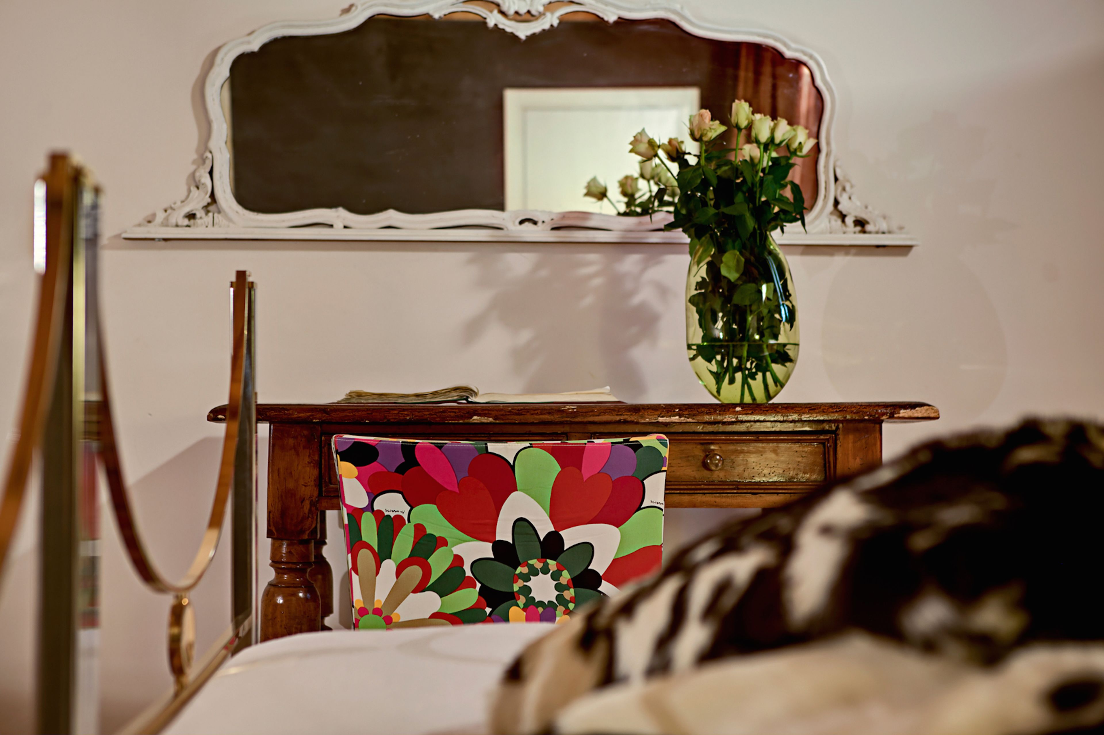 Una camera da letto con un comò in legno, uno specchio e un vaso con fiori.
