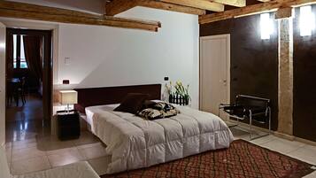 Une chambre avec un grand lit, une table de chevet avec une lampe, un tapis rouge à motifs et une chaise noire.