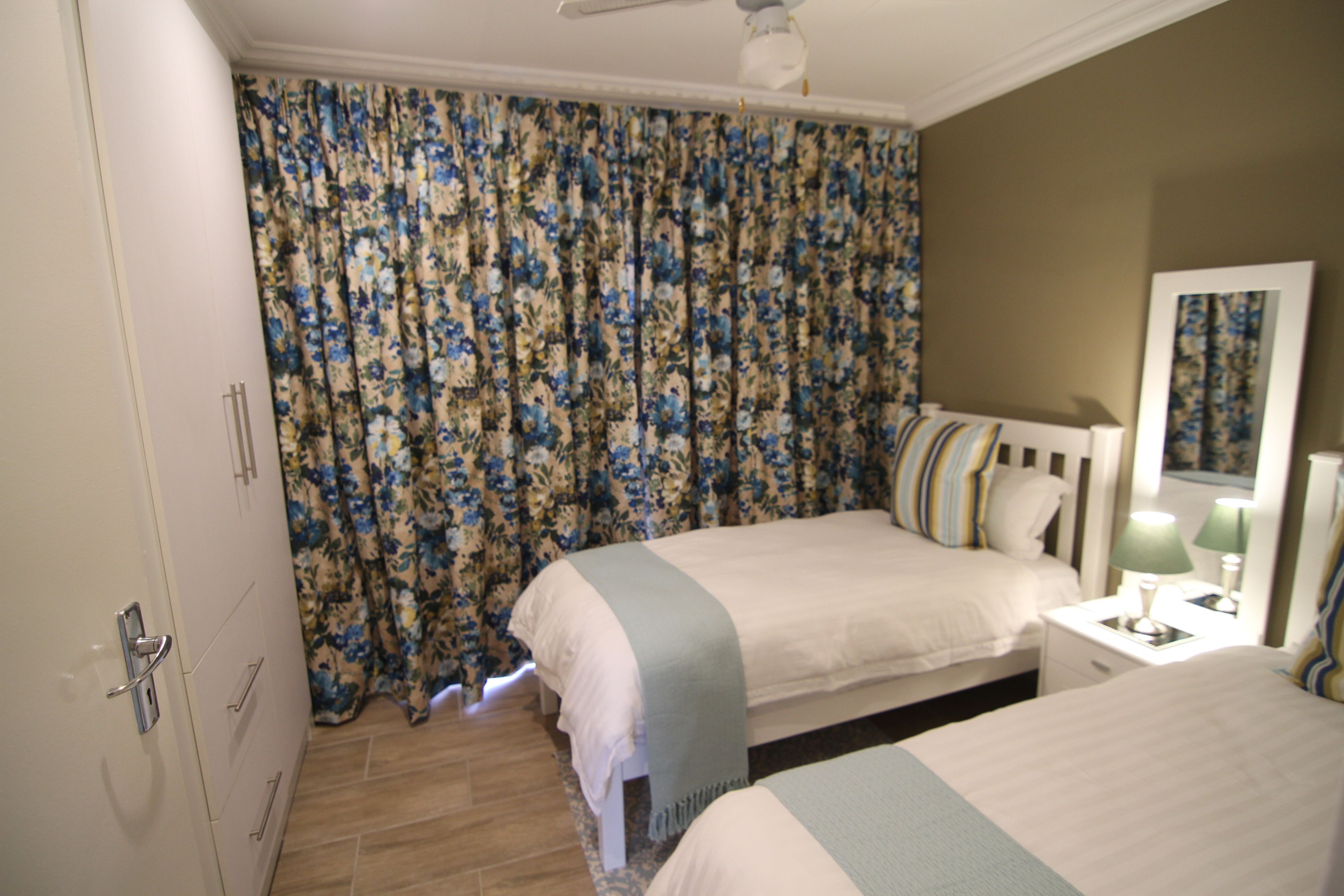 A bedroom with two beds, a wardrobe, a nightstand with a lamp, and a mirror.