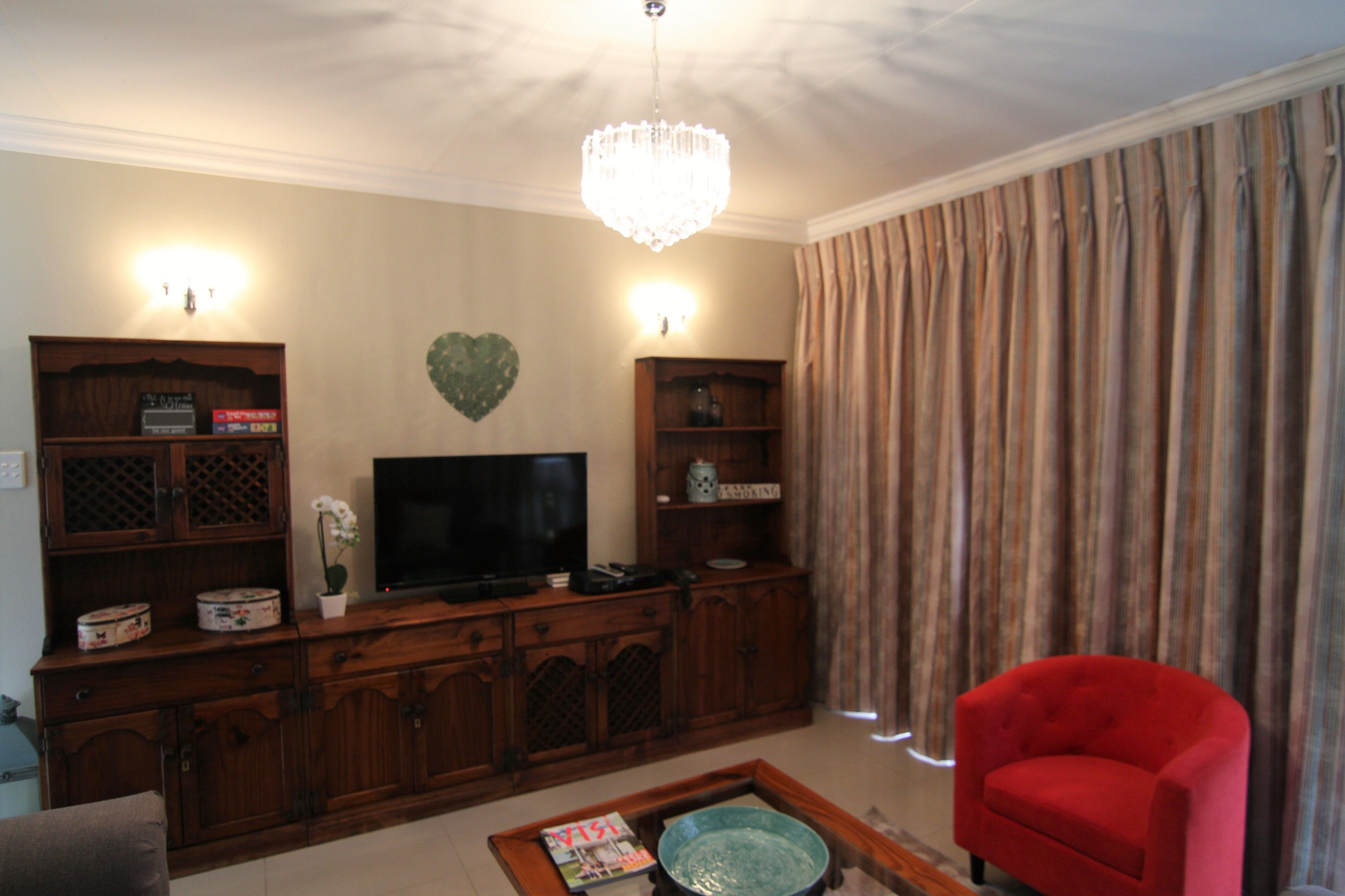 Una sala de estar con televisor, mueble bajo de madera, sillón rojo y una araña.