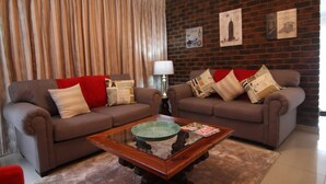 A living room with two sofas, a coffee table, and a brick wall with framed pictures. - Hesperus Street (Alberton)