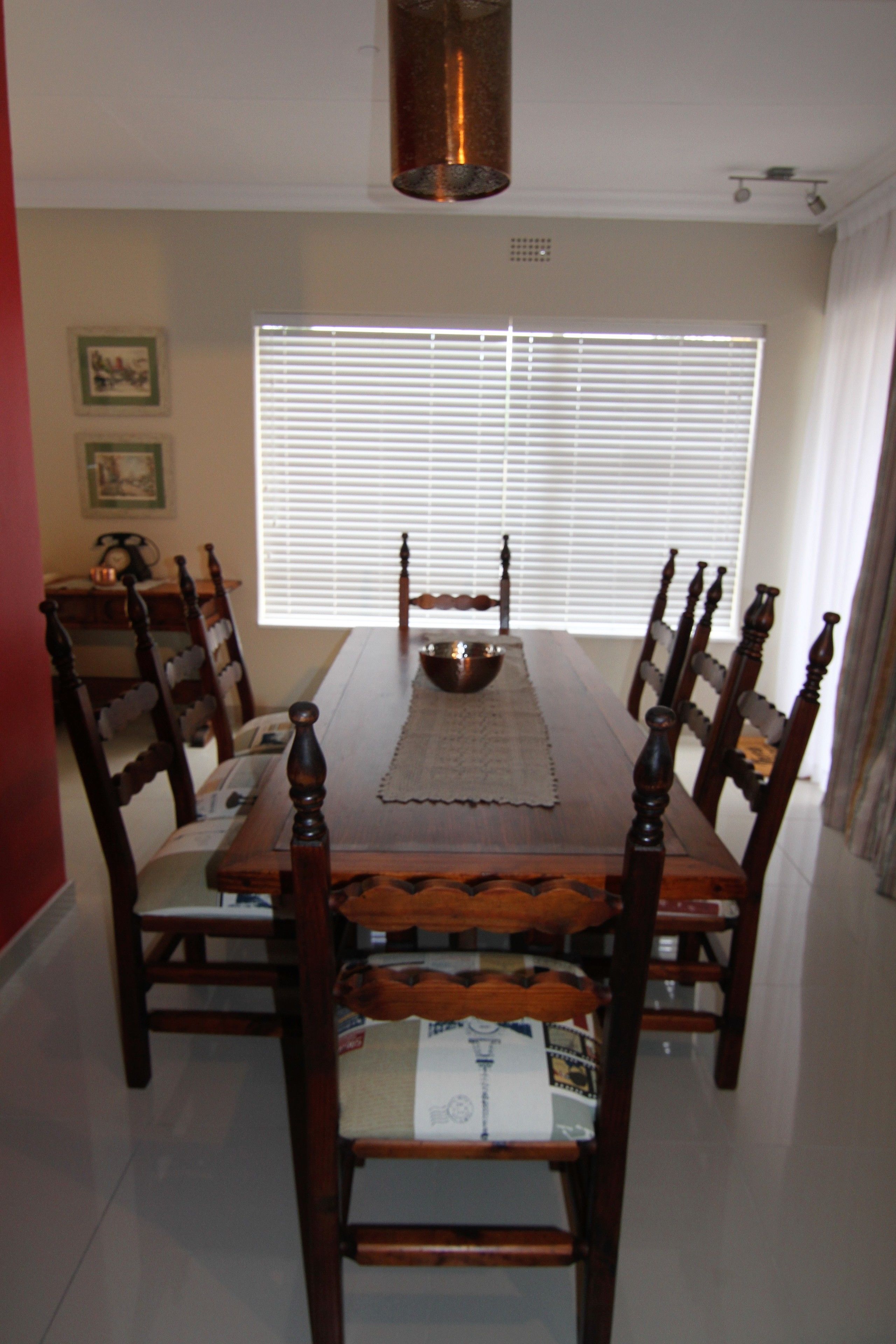 A dining room with a wooden table and chairs, a chandelier, and a window with blinds.