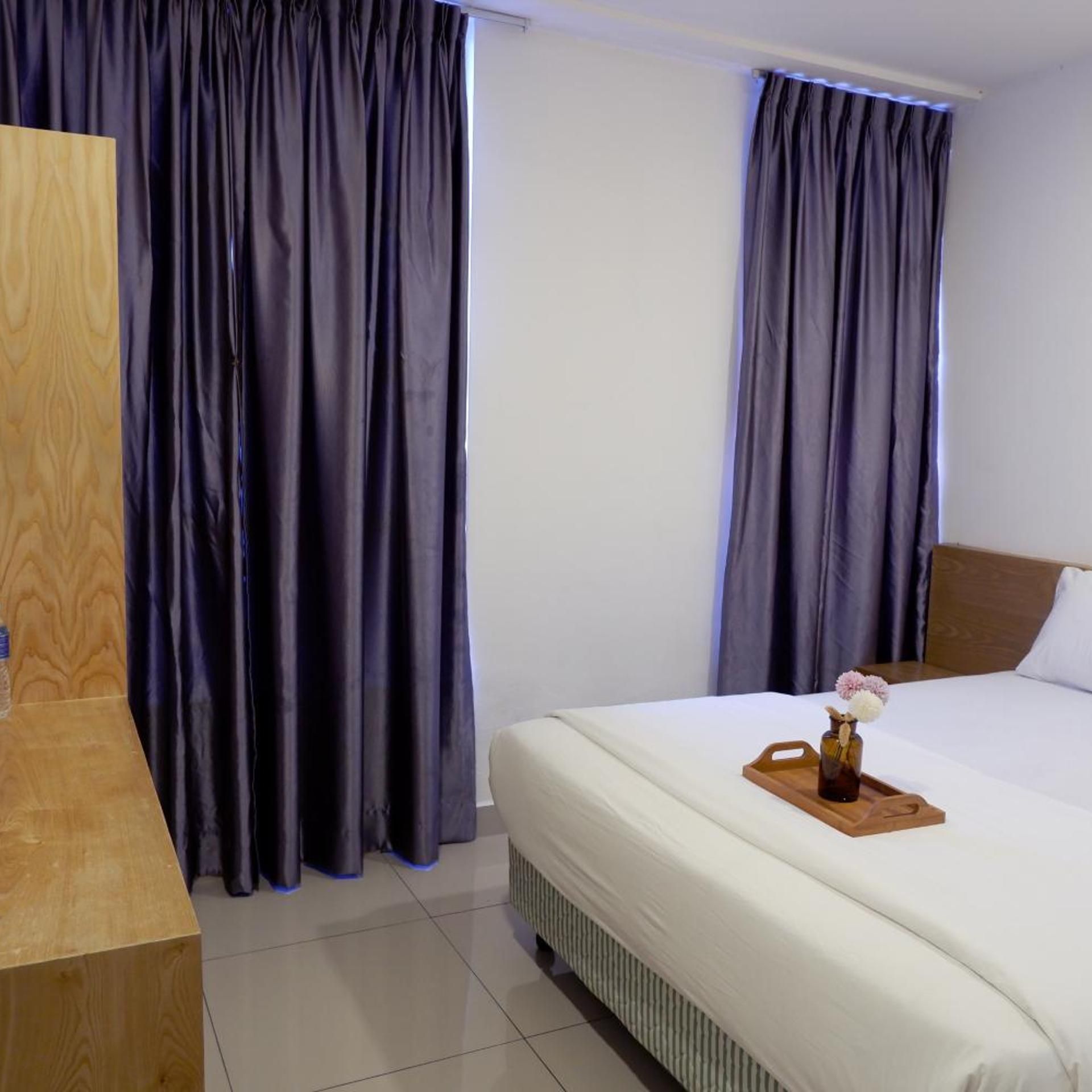 A hotel room with a bed, a wooden nightstand, and a window with curtains.