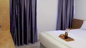 A hotel room with a bed, a wooden nightstand, and a window with curtains.