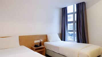 Habitación de hotel con dos camas, una mesita de noche y una ventana con cortinas.
