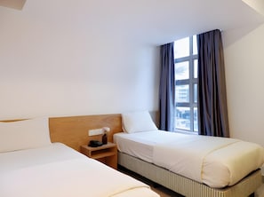 Een hotelkamer met twee bedden, een nachtkastje en een raam met gordijnen.