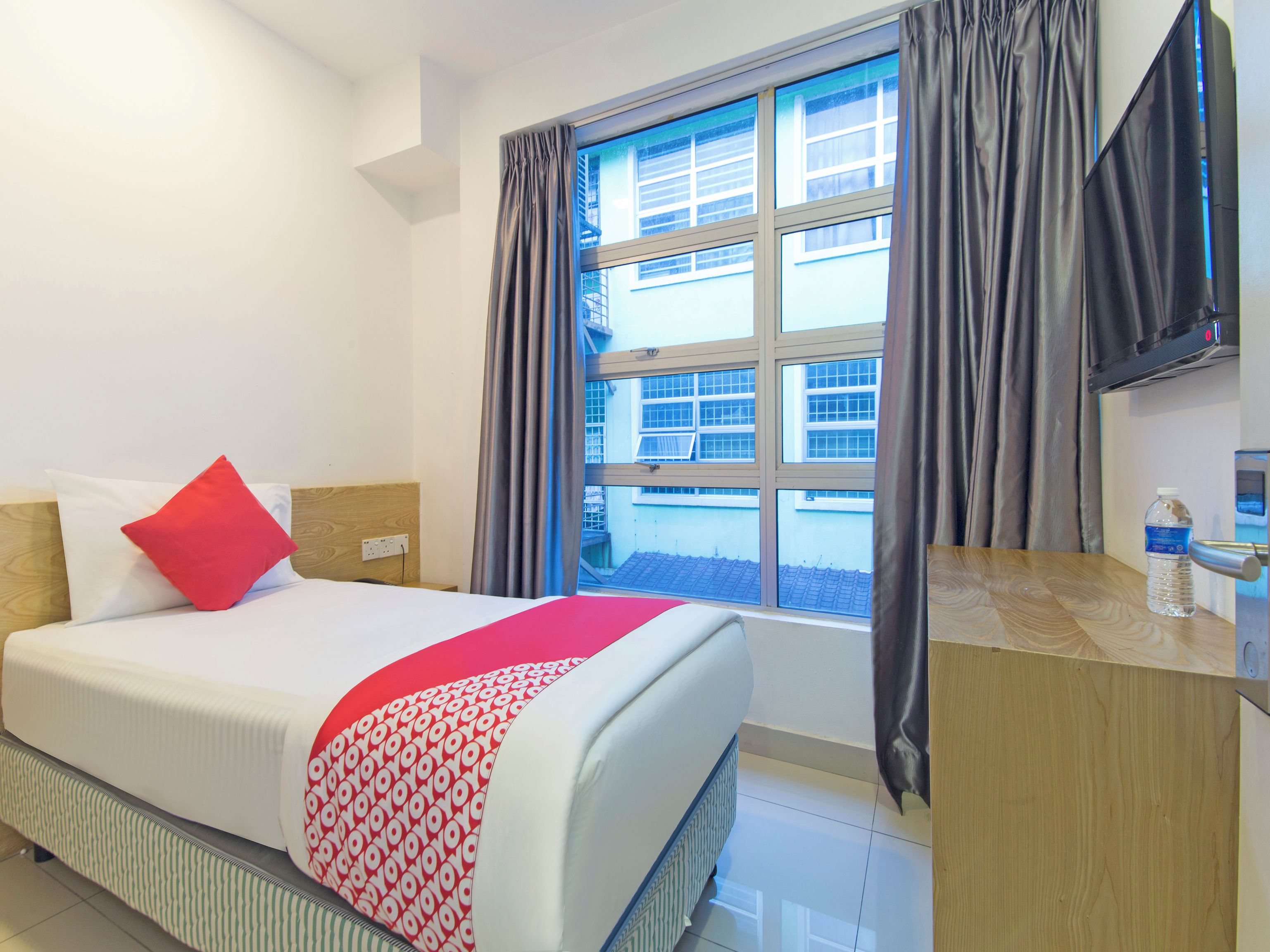 Habitación de hotel con cama, escritorio, ventana con cortinas y televisor.