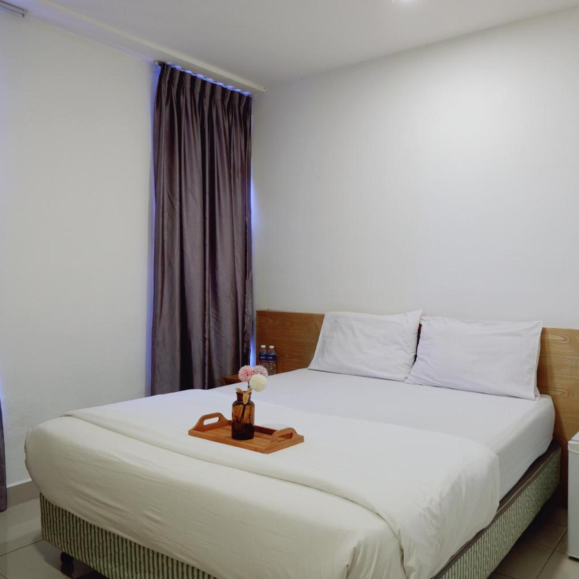 A hotel room with a bed, a wooden headboard, a nightstand, and a tray with a vase of flowers.