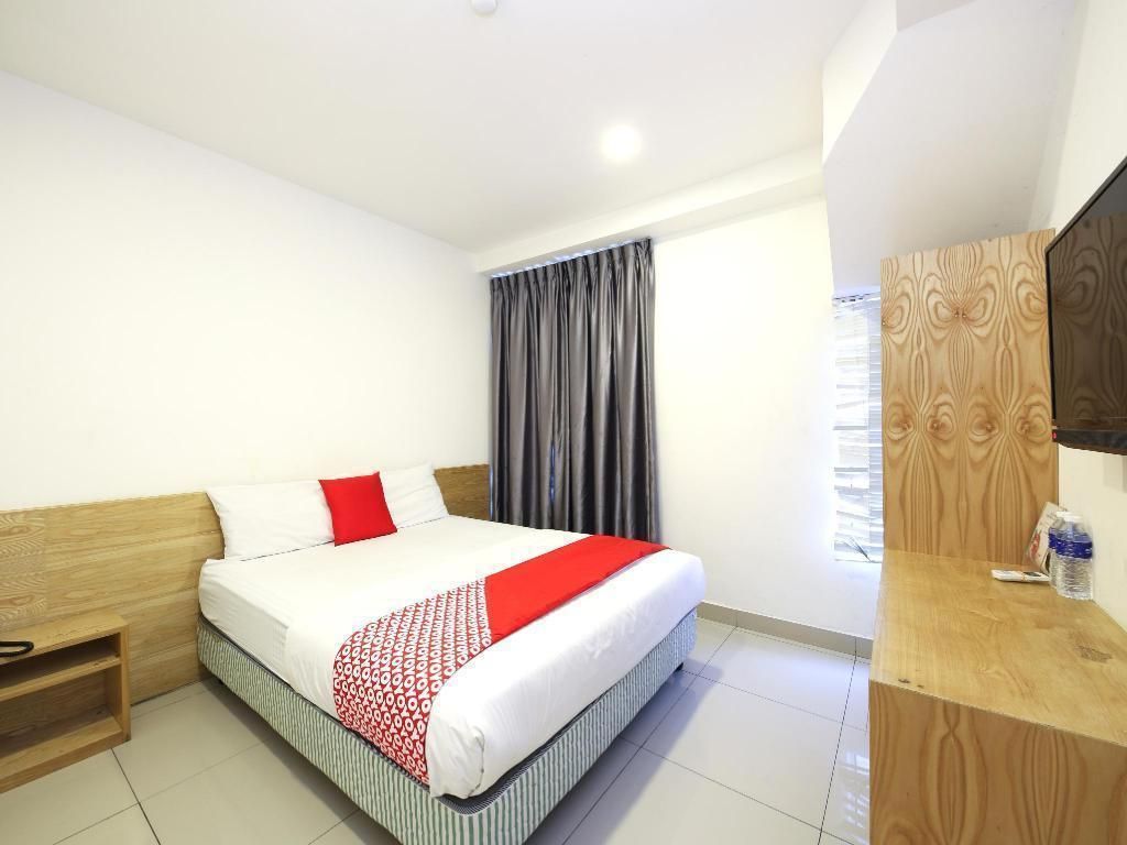 Habitación de hotel con cama, cabecera de madera, mesita de noche, espejo y ventana con cortinas.