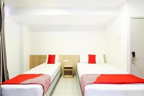 A hotel room with two single beds, each with a red pillow and a white bedspread. There is a small wooden nightstand between the beds. - Iris Hotel (Kajang)