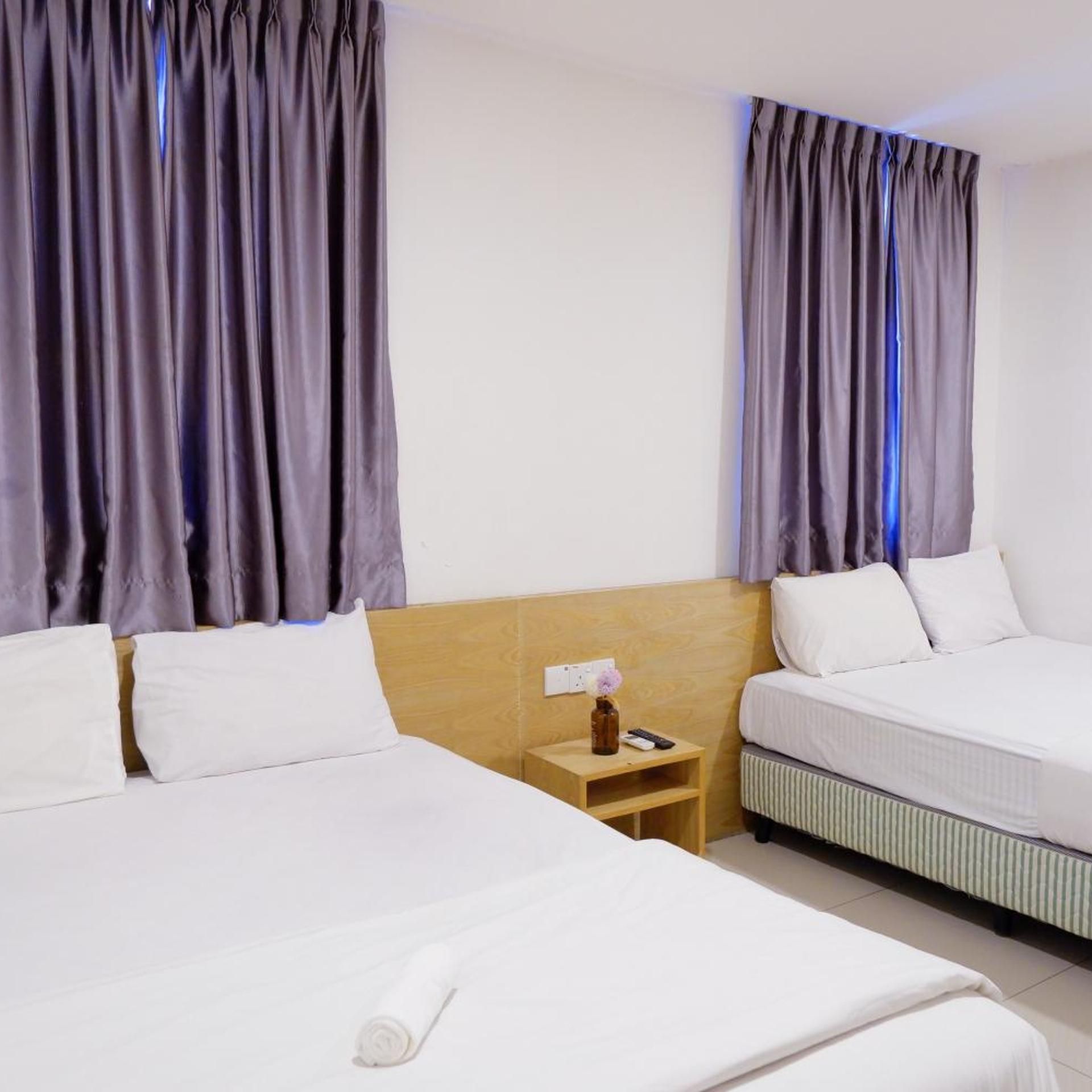 A hotel room with two beds, a wooden headboard, a nightstand with a vase and remote control, and curtains.