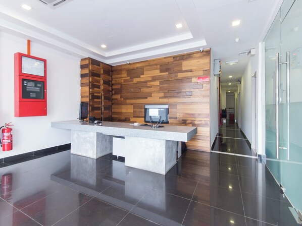 A reception desk with a wooden panel wall, a fire alarm, and a glass door leading to a corridor. - Iris Hotel (Kajang)