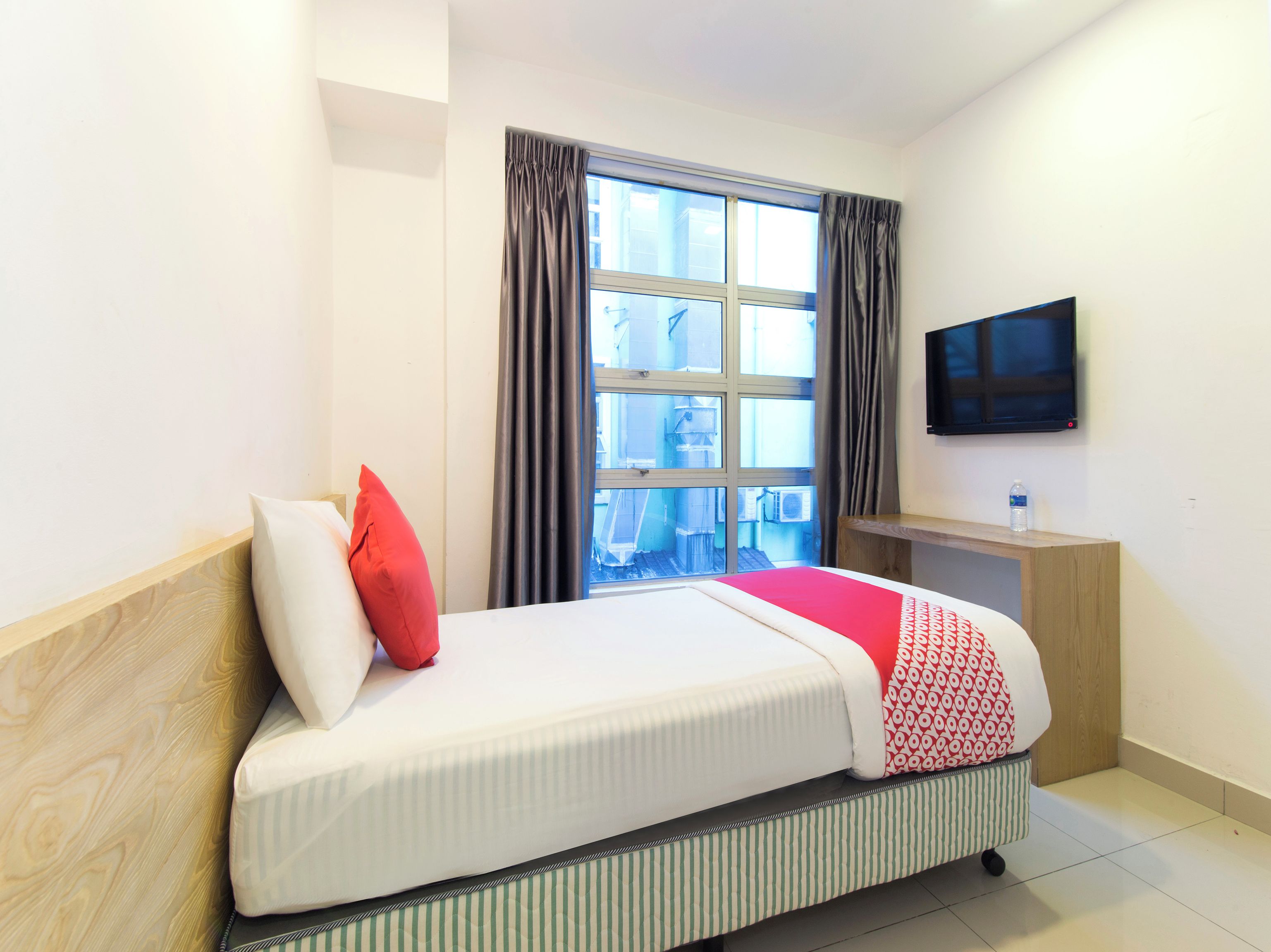 Una habitación de hotel con una cama, un televisor montado en la pared y un ventanal con cortinas.