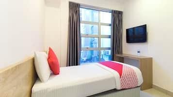 Una habitación de hotel con una cama, un televisor montado en la pared y un ventanal con cortinas.