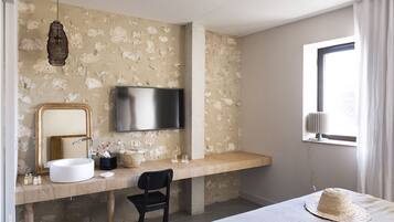 A modern bathroom with a large mirror, a sink, a television, and a window with curtains.