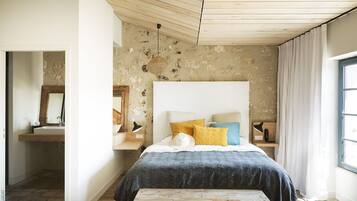 Un dormitorio con una cama grande, techo de madera, pared de piedra y una ventana con cortinas.