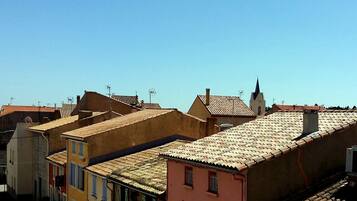 A row of terracotta-roofed buildings with uniform architecture, a clear blue sky, and a church steeple in the background.