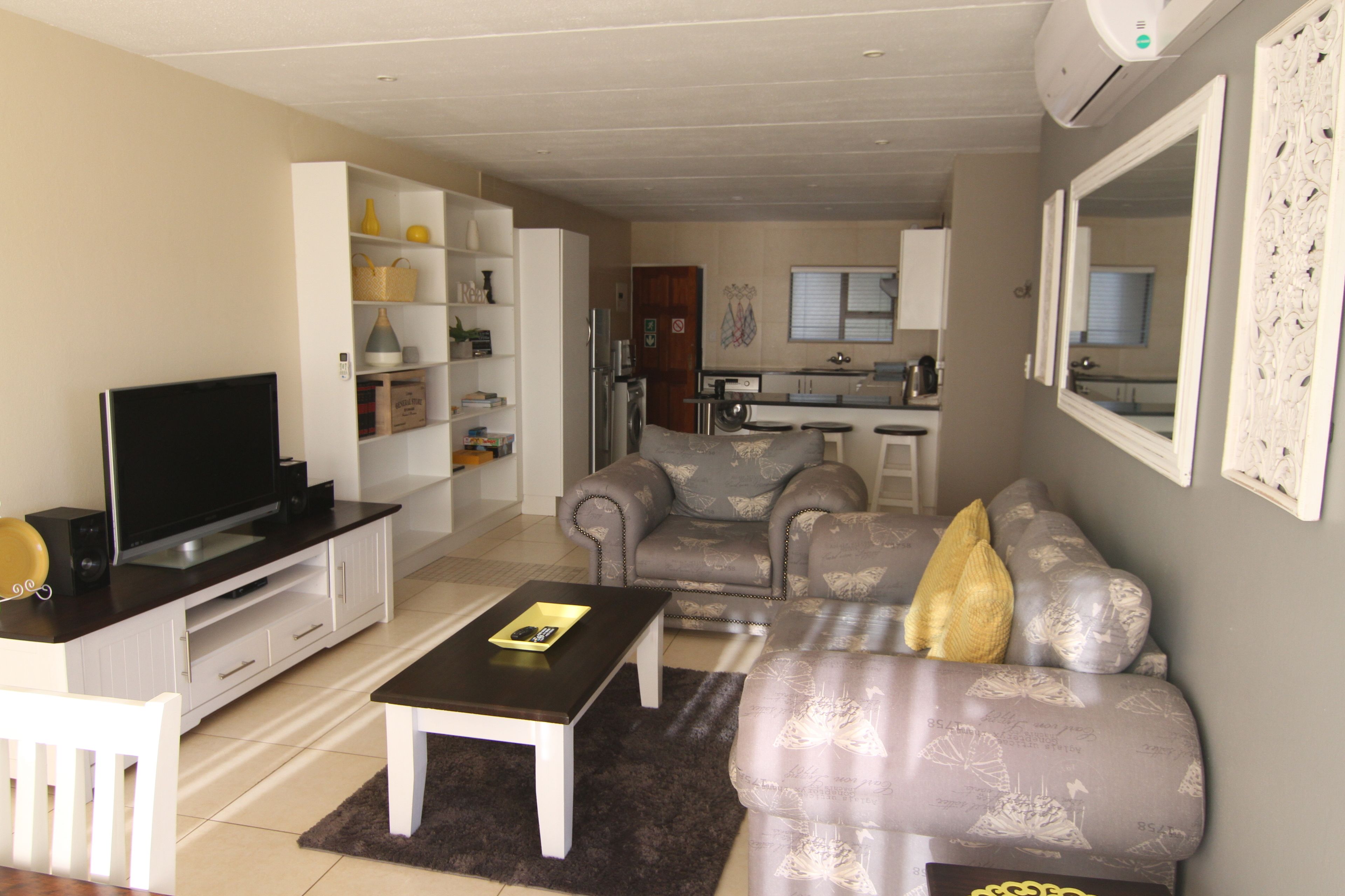 A living room with a TV, sofa, and coffee table. There is a kitchen in the background.