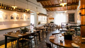 L’intérieur d’un restaurant, avec de nombreuses tables, des chaises, des bouteilles de vin exposées sur des étagères, des tableaux encadrés accrochés au mur et des lampes suspendues.