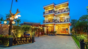 A multi-story hotel with a traditional architectural style, featuring balconies and a well-lit entrance. - CIC Hoi An Villa (Da Nang)
