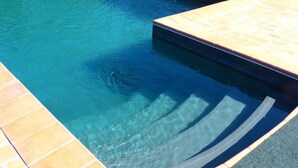 En klar, blå pool med flisekant og træterrasse.