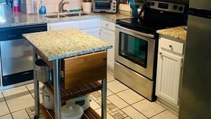 Eine moderne Küche mit weißen Schränken, Edelstahlgeräten und einem Holztisch mit Metallgestell.